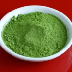 Ceremonial grade matcha powder in a bowl with a traditional bamboo whisk and hot water