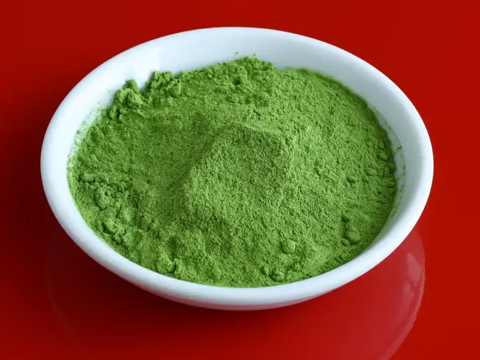 Ceremonial grade matcha powder in a bowl with a traditional bamboo whisk and hot water