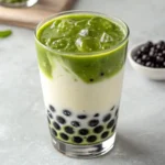 A tall glass of matcha milk tea with boba pearls and ice, served with a metal straw.